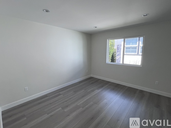 A room with wooden flooring and a window showing a building and trees outside.