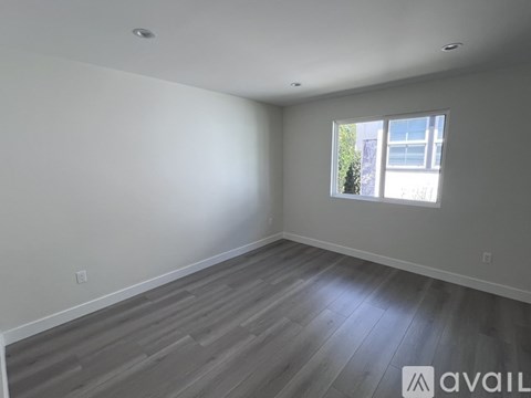 A room with wooden flooring and a window showing a building and trees outside.