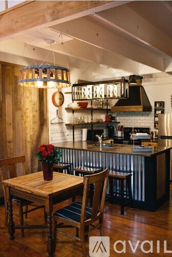 A wooden table with chairs and a vase of flowers in front of a kitchen counter.