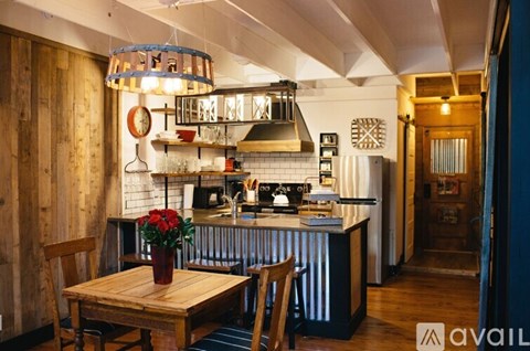A kitchen with a wooden table and chairs, a hanging light fixture, and a vase of red roses on the table.