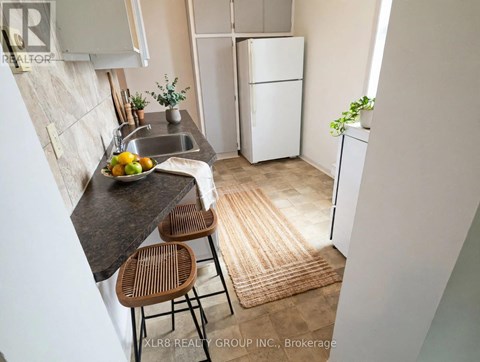 A kitchen with a sink, a refrigerator, and a counter with a bowl of fruit on it.