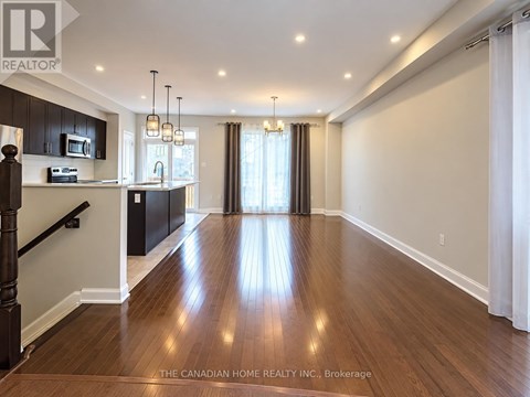 A spacious room with wooden floors and a kitchen area with black cabinets and a microwave.