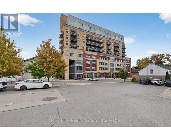A white car is parked in a lot in front of a multi-story apartment building.