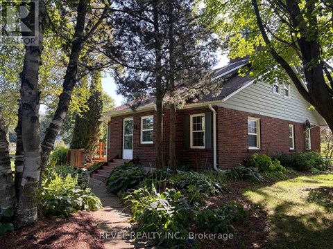 A house with a red brick exterior and a white trim is surrounded by trees and plants.
