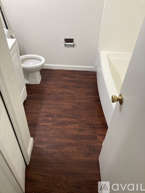 A white toilet sits in a small bathroom with wooden floors.