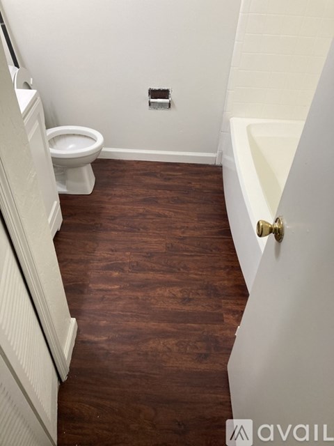 A white toilet sits in a small bathroom with wooden floors.