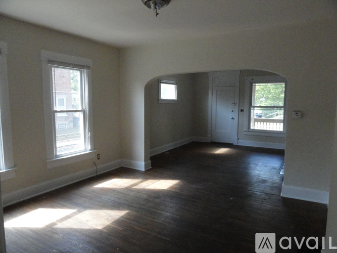 A room with wooden floors and white walls, with a window on the left and a door on the right.