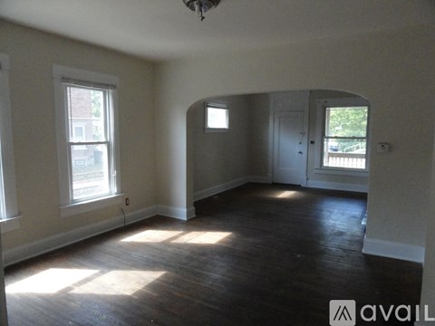 A room with wooden floors and white walls, with a window on the left and a door on the right.