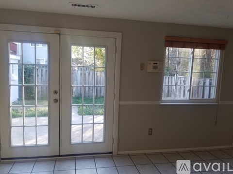 A room with two doors and a window with a view of a fence and trees.