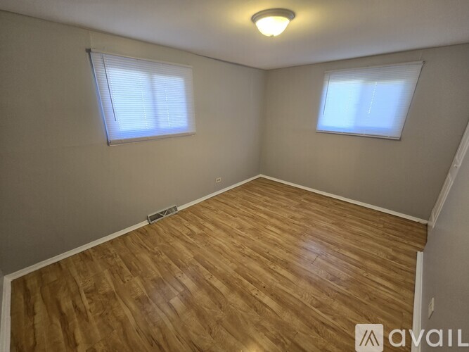 A room with wooden flooring and two windows.
