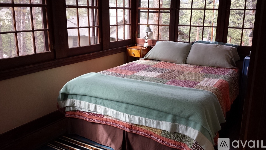 A bed with a green blanket and pillows in a room with wooden windows.