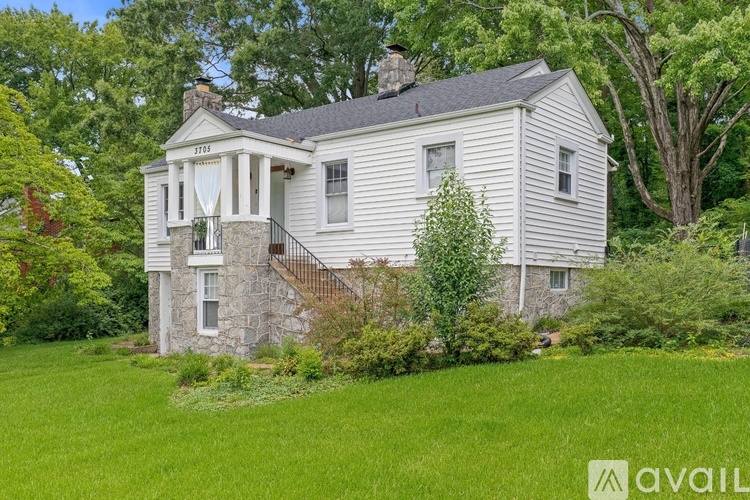 A house with a stone foundation and a chimney is surrounded by greenery.