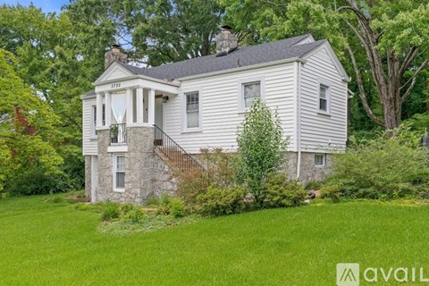 A house with a stone foundation and a chimney is surrounded by greenery.