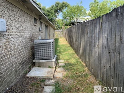 A backyard with a wooden fence and a brick house with an air conditioning unit.