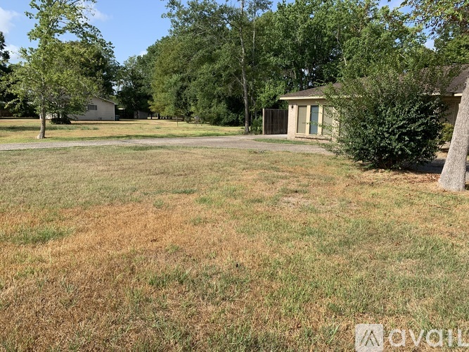 A grassy field with a house and trees in the background.