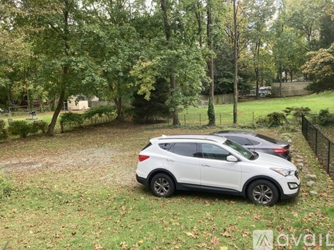 A white car is parked in a grassy area with trees in the background.