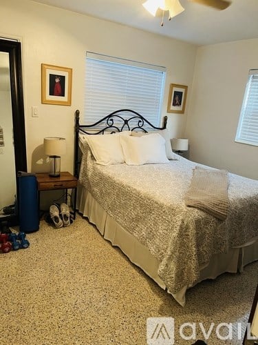 A bedroom with a bed, nightstand, and two windows.