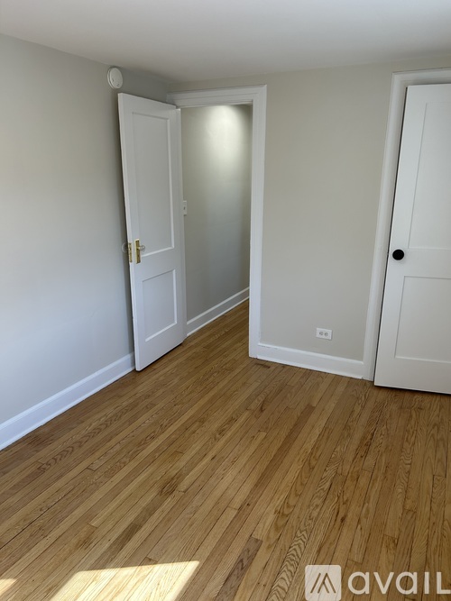 A room with wooden floors and white walls, featuring two doors and a window.