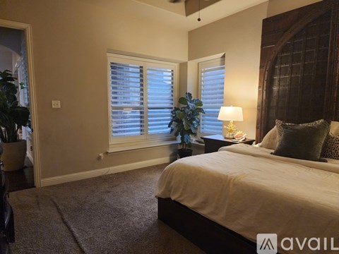 A bedroom with a bed, a nightstand with a lamp, and a window with blinds.