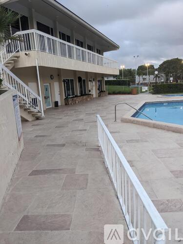 A pool area with a white fence and a building in the background.