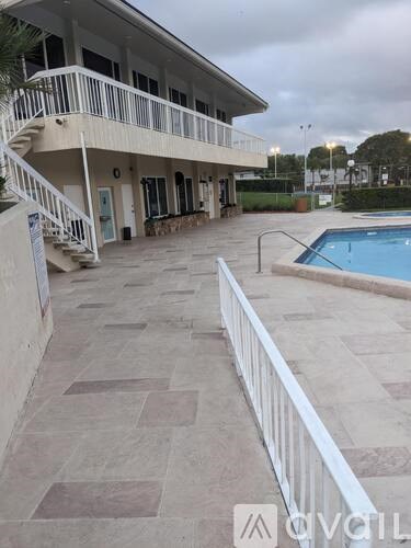 A pool area with a white fence and a building in the background.