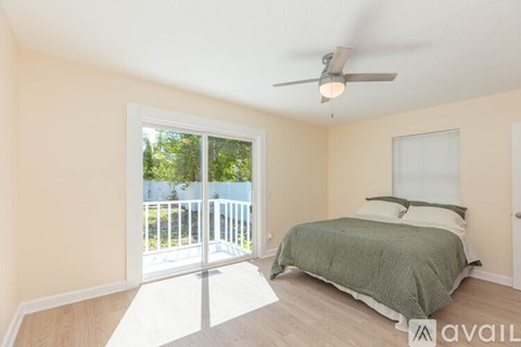 A bedroom with a bed, a ceiling fan, and a sliding glass door leading to a balcony.