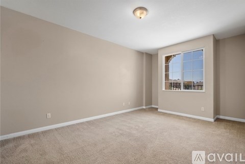 A room with beige walls and carpeting, a window with a view of the outside, and a light fixture on the ceiling.