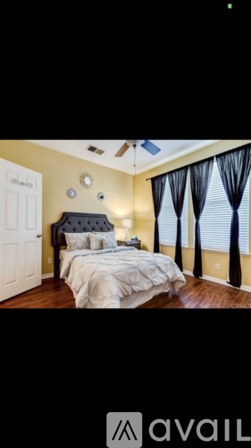 A bedroom with a bed, a window with black curtains, and a white door.
