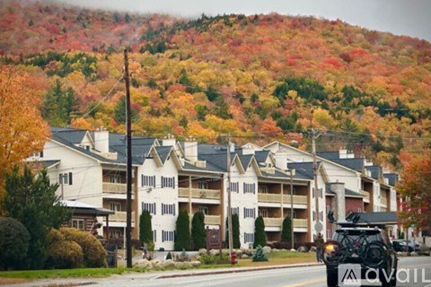 A row of apartment buildings in front of a hill with fall foliage.