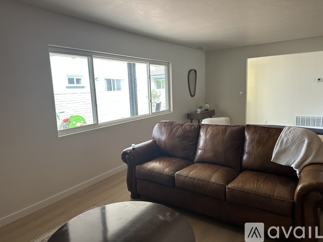 A brown leather couch sits in a living room with a large window behind it.