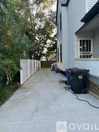 A white house with a black trash bin on the concrete walkway.