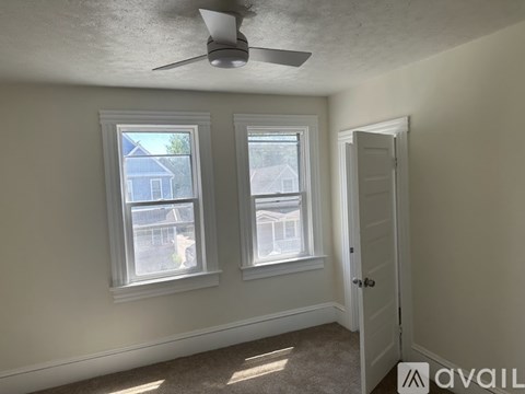 A room with a ceiling fan and two windows.