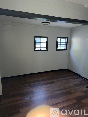 A room with wooden flooring and two windows.