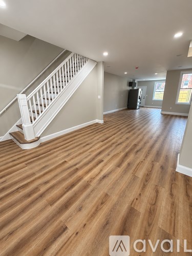 A spacious room with wooden flooring and a staircase.