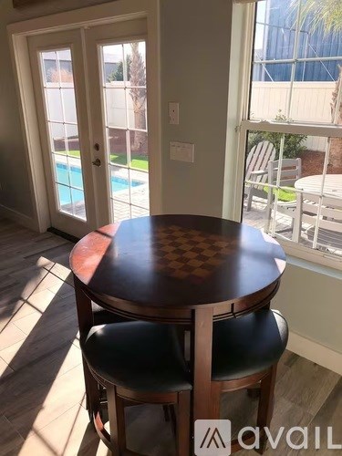 A table with two chairs in front of a window with a pool in the background.