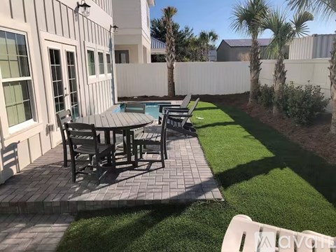 A patio with a table and chairs is surrounded by a white fence and palm trees.