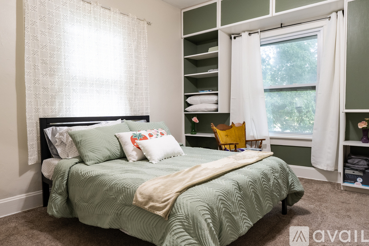 A bedroom with a bed, a window with curtains, and a shelf with towels and a purple stuffed animal.