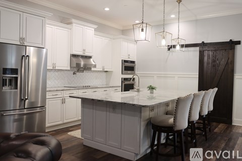 A kitchen with white cabinets and a large island with chairs around it.