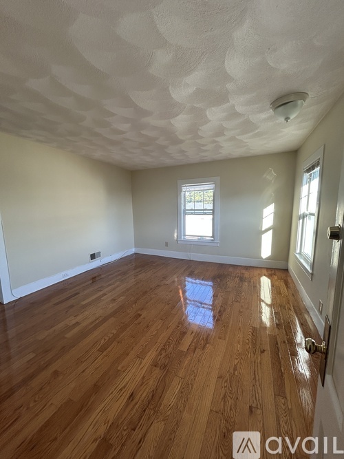 A room with wooden flooring and a window letting in sunlight.