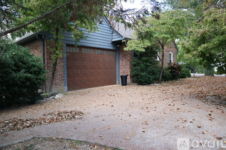 A house with a brown garage door surrounded by trees and fallen leaves.