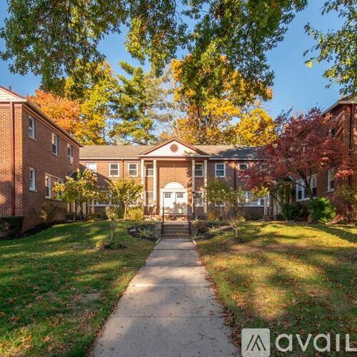 A tree-lined walkway leads to a brick building entrance.