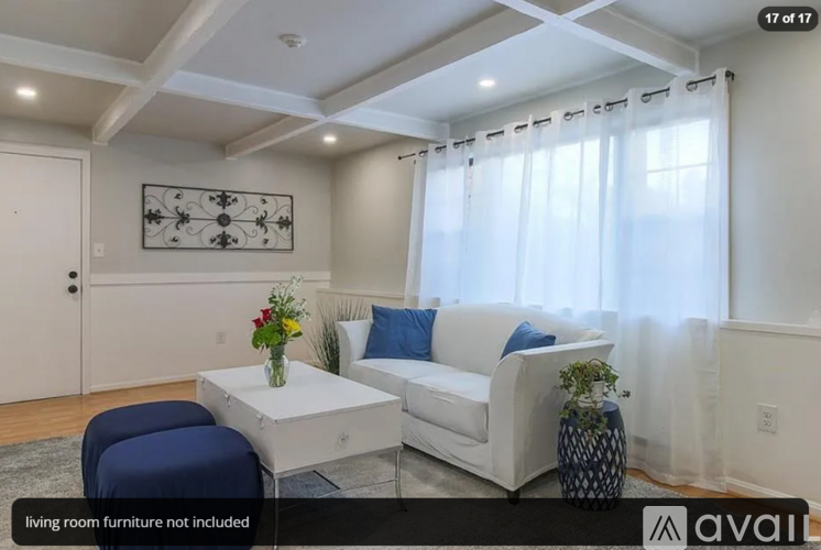 A living room with white furniture and a large window with white curtains.