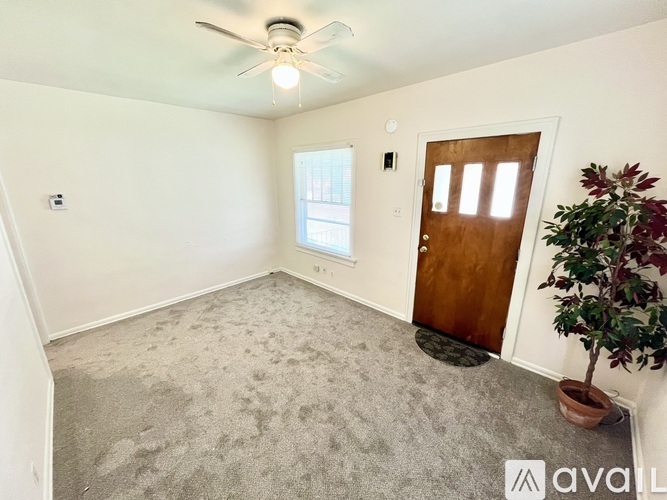 A room with a carpeted floor, a ceiling fan, and a door.