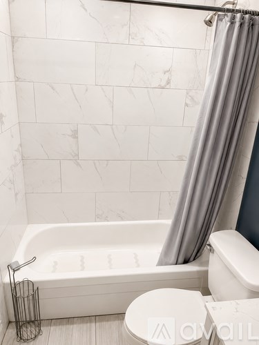 A white bathroom with a tub, toilet, and a shower curtain.