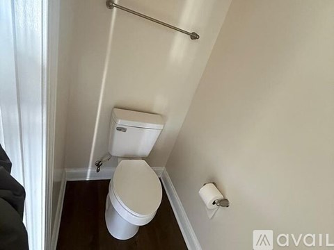 A white toilet in a small bathroom with a roll of toilet paper on the wall.