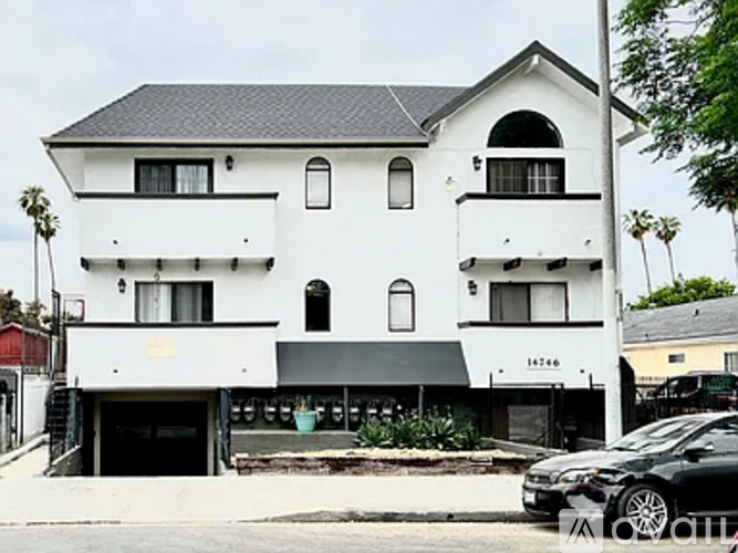 A white two-story building with black roofing and a black car parked in front.