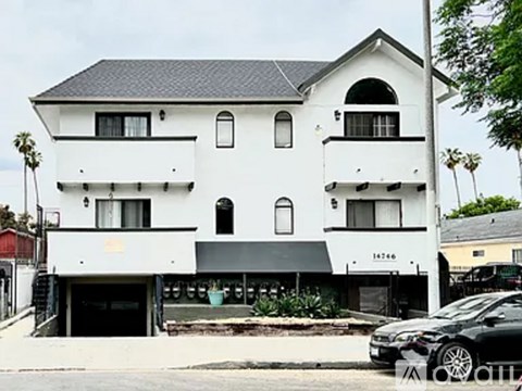A white two-story building with black roofing and a black car parked in front.
