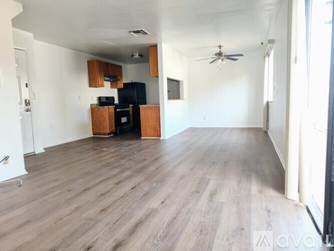 A spacious room with wooden flooring and a black refrigerator.