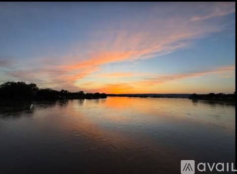 A serene sunset over a calm body of water with trees in the distance.