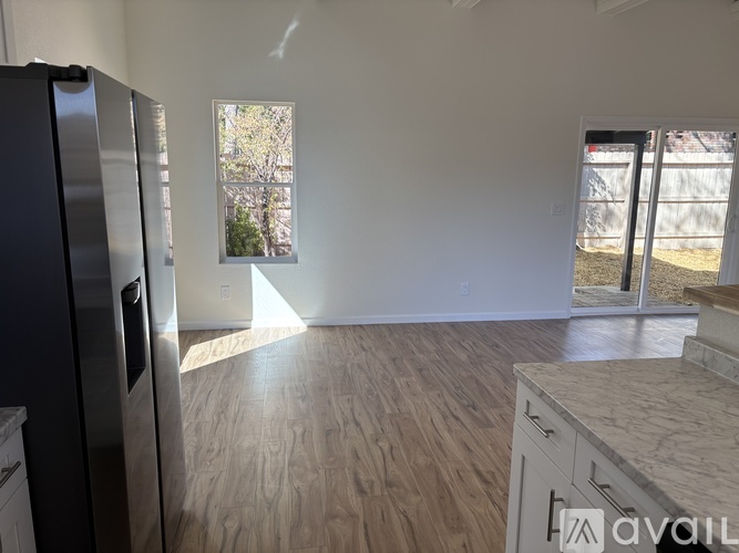 A kitchen with a refrigerator, wooden flooring, and a window with a view of trees.